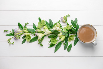 Beautiful flowers and cup of coffee on white wooden background