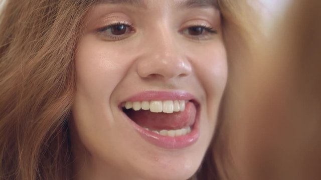 Happy woman licking white teeth with tongue front bathroom mirror in home