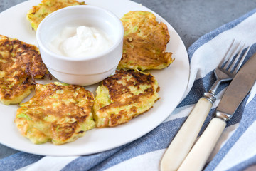 vegetable pancakes, squash pancakes with sour cream on a plate, fork, knife, towel