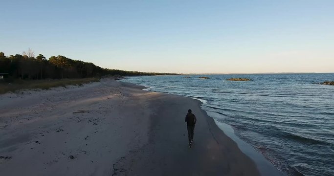 Aerial Shot of a Man Running By The Östersjö Ocean in The Evening at The Ystad Saltsjöbad Beach With The Horizon of South Sweden Skåne in The Background