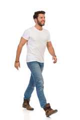 Handsome Man In White T-shirt, Jeans And Boots Is Walking And Smiling