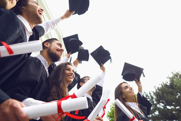 Happy graduates raised their hands with scrolls of diplomas