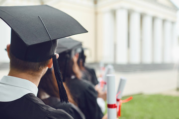 Scrolls of diplomas in the hands of a group of graduates.