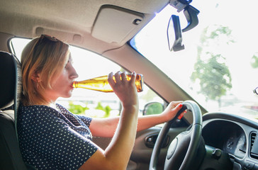 drunk girl driving a car. Girl drinks alcoholic beer from a bottle while driving