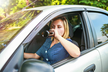 drunk girl driving a car. The girl drinks alcohol from a bottle while driving