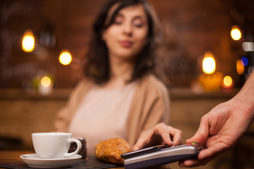 Photo of attractive woman paying with mobile phone using wireless payment on a coffee shop