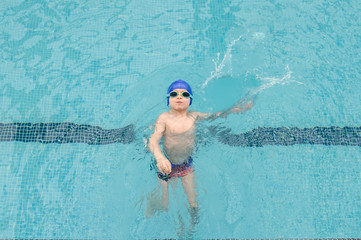 top view of a 7-year boy swimming backstroke in a swimming pool