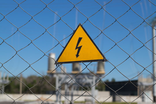 Electrical hazard sign on metal grid. On the background of unfocused high-voltage electrical substation. Concept: danger of electric current, death from electric shock