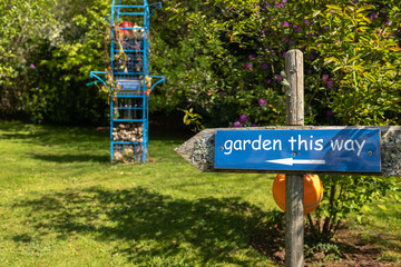 A blue sign post in garden directing the way, lots of green and blue, nobody in the image