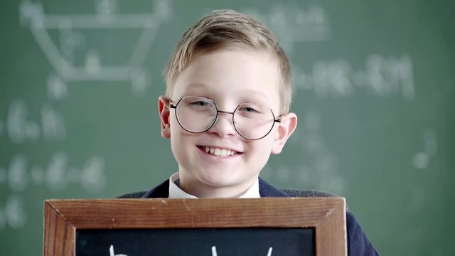 schoolboy covering face with black board with back to school lettering and smiling while looking at camera 