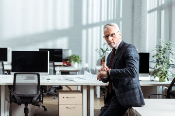 handsome businessman in glasses touching watch in modern office