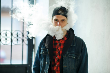 Vape teenager. Portrait of young handsome guy in a cap smoking an electronic cigarette on the...