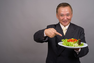 Portrait of mature Asian businessman against gray background