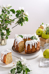 Piece of homemade apple cake with cinnamon and icing on white background with flowering apple branches. Spring mood. Bakery, confectionery concept. Top view, copy space