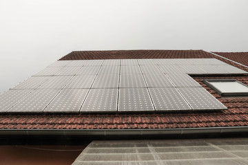 Solar panels on a roof with red tiles, cloudy sky