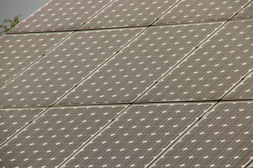 Solar panels on a roof with red tiles, cloudy sky