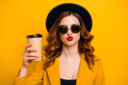 Close up photo beautiful funky dreamy she her lady send air kiss flirty vacation hot beverage takeout paper container hand arm wear specs formal-wear suit isolated yellow bright background