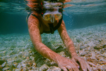 Woman snorkeling underwater. Female swimmer with diving mask and snorkel touching stones at bottom...
