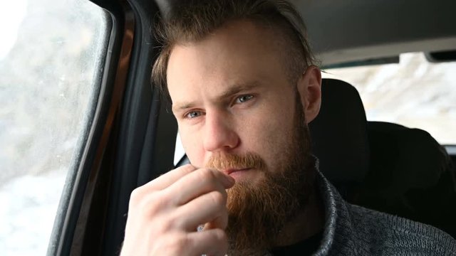 Close-up portrait of a smiling bearded hipster male with a toothpick in his mouth sitting in the car in the backseat and reflecting on the sides