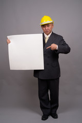 Mature Asian construction businessman against gray background