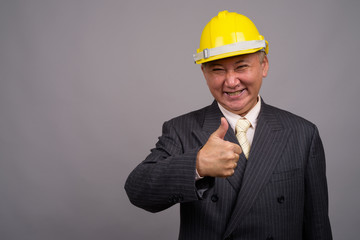 Mature Asian construction businessman against gray background