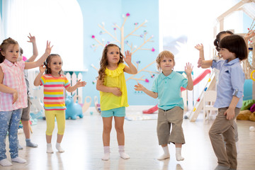 Happy children having fun dancing indoors in a sunny room at day care or entertainment center