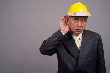 Mature Asian construction businessman against gray background