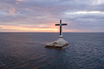 Catholic cross in a flooded cemetery in the sea near the island of Camiguin. Sunset over the sea. Cross on the flooded cemetery. Tourist place in the Philippines.