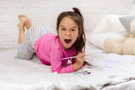 Cute Little Girl Drawing Pictures While Lying On Bed. Kid Painting At Home