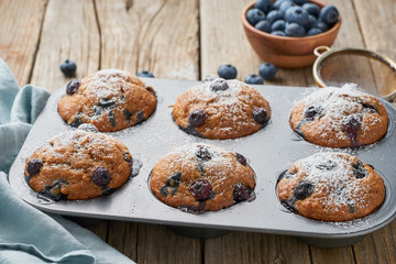Blueberry muffin in tray, side view. Cupcakes with berries in baking dish on old linen napkin, rustic wooden table, breakfast with cake