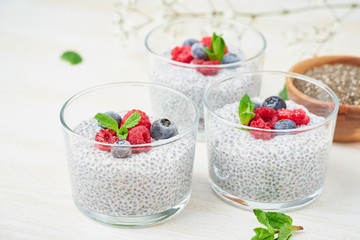 Chia pudding with fresh berries raspberries, blueberries. Three glass, light wooden background, side view, flowers, close up.