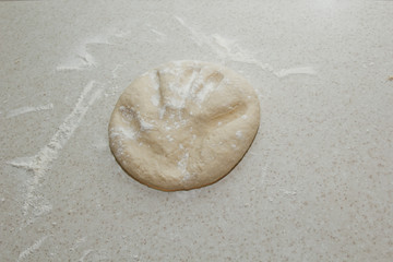 Obraz premium A pile of kneaded dough sprinkled with wheat flour is lying on a white kitchen table. Top view. baking, cooking