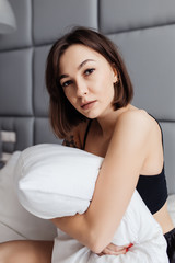 Side view of attractive young smiling woman sitting in bed and hugging a pillow