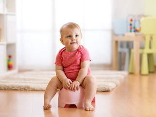 Little smiling baby girl sitting on a pot. Isolated on white background.