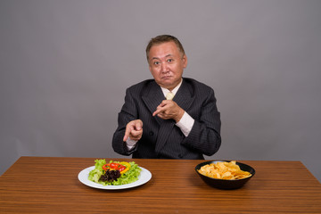 Mature Asian businessman sitting with wooden table against gray 