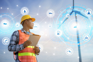Male Engineer holding tablet with save world icons in Wind Mill Power Generator Station with orange safety hat and wind turbines on background.