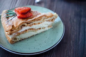 A piece of handmade cake  with custard and a cup of coffee on a brown table.