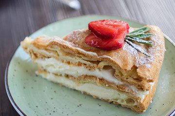 A piece of handmade cake  with custard and a cup of coffee on a brown table.