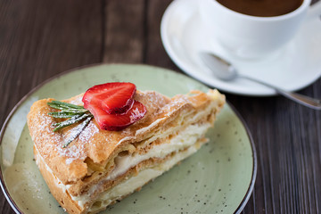 A piece of handmadeм cake  with custard and a cup of coffee on a brown table.