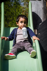 Adorable baby with a milk bottle playing in the playground outdoor