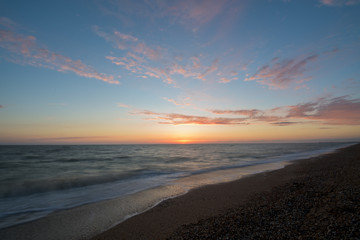 Fototapeta na wymiar photo on long exposure, waves at sea at sunset. pink sunset