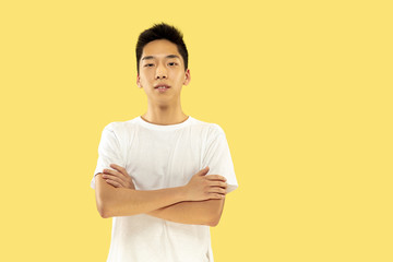 Korean young man's half-length portrait on yellow studio background. Male model in white shirt. Standing and looking. Concept of human emotions, facial expression. Front view. Trendy colors.