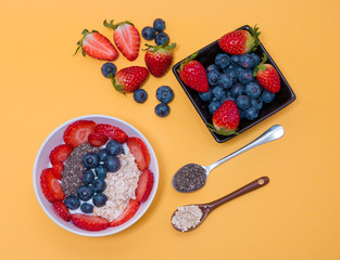 Desayuno saludable. Bol de yogur de soja con fresas, arándanos, avena y chia en fondo amarillo.