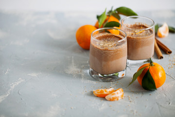Glass of hot tangerine orange cocoa or chocolate decorated citrus peel on gray background with copy...