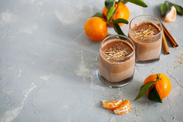 Glass of hot tangerine orange cocoa or chocolate decorated citrus peel on gray background with copy...