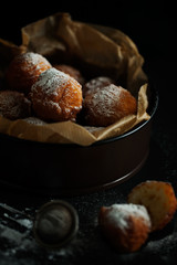 A portion of delicious fresh deep-fried cheese donuts decorated with powdered sugar on a black table. Fresh homemade pastry on a dark background close-up. Selective focus