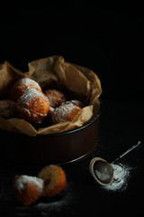 A portion of fresh deep-fried and decorated with powdered sugar cottage cheese donuts hole on baking paper. Fresh homemade cakes on a dark background close-up. Selective focus
