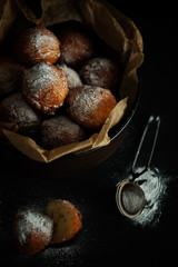 A portion of delicious fresh deep-fried cheese donuts decorated with powdered sugar on a black table. Fresh homemade pastry on a dark background close-up top view. Selective focus