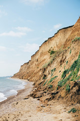 Fototapeta na wymiar Beautiful sandy cliff with grass and sea waves on beach with on tropical island. Big rock and waves in ocean bay or lagoon. Tranquil calm moment. Summer vacation. Copy space