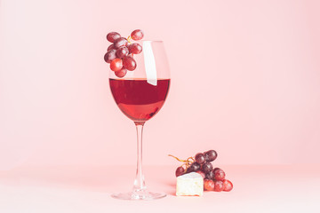 A glass with red wine and snack on a delicate pink background. Selective focus. Copy space. Minimalism